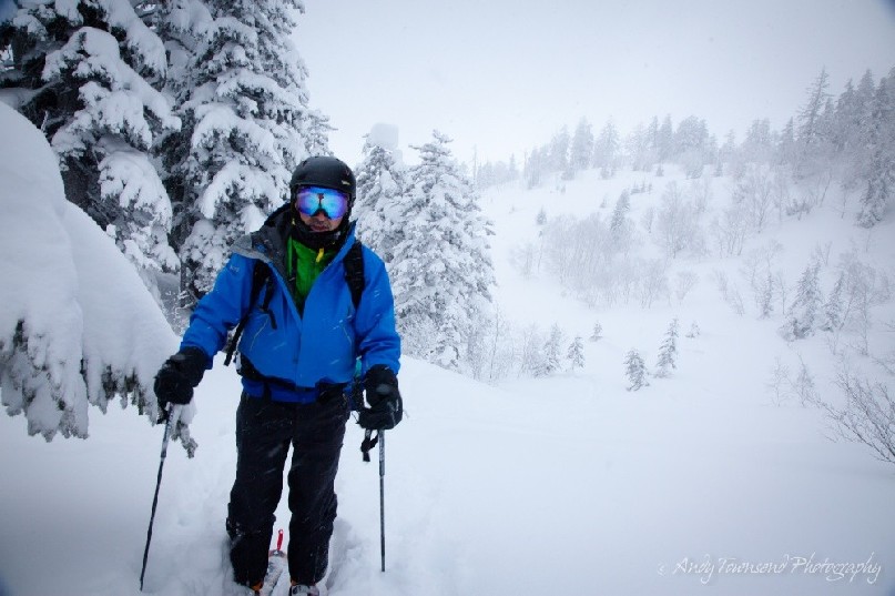 A backcountry skier pauses for breath after making their way up a valley of snow-laden trees near Tokachidake ski area.