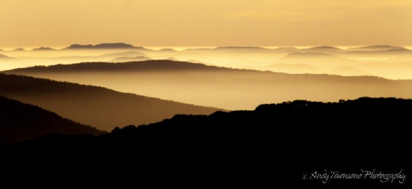 Mist hangs in the valleys between the ridgelines as the sun rises.