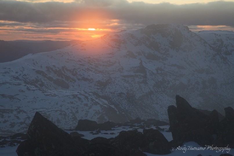 The sun sets through fine cloud causing an orange glow above the distant ranges of Naturalist Peak and Mt Field West.