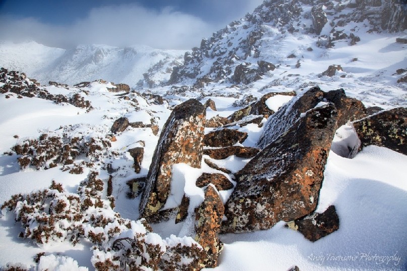 A clearing fog reveals snow-covered boulders and the distant peak of Mt Florentine.