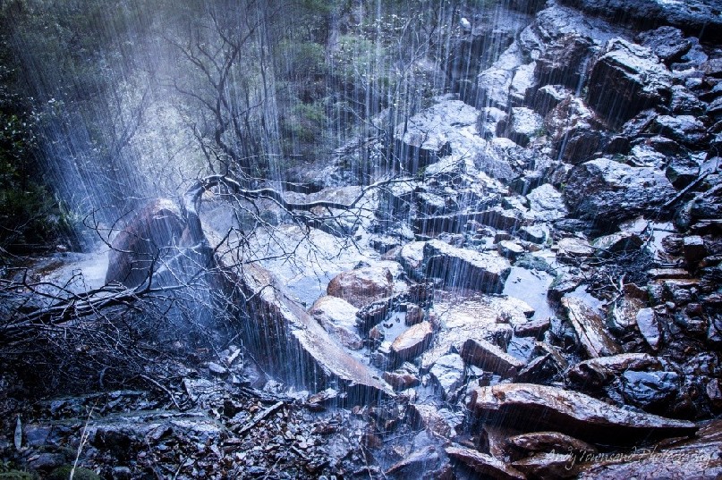 Looking down on a jumble of rocks as a cascade of water falls over the viewer.