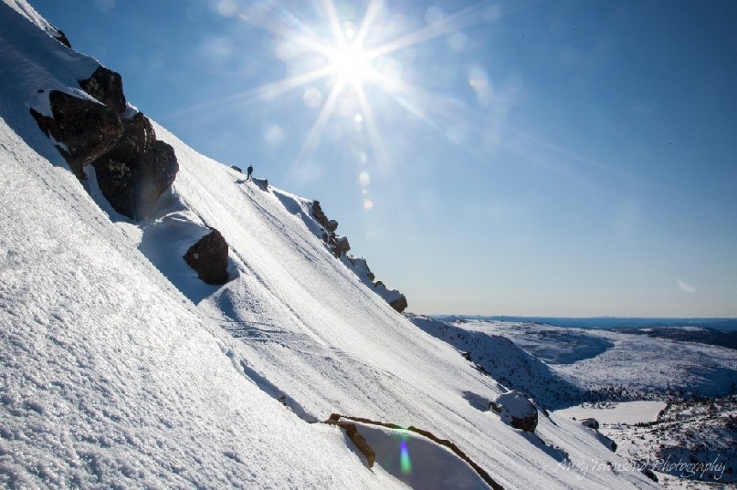 Clear blue skies and a bright sun over a distant snowshoer as they descend a step snow slope on the Rodway range.