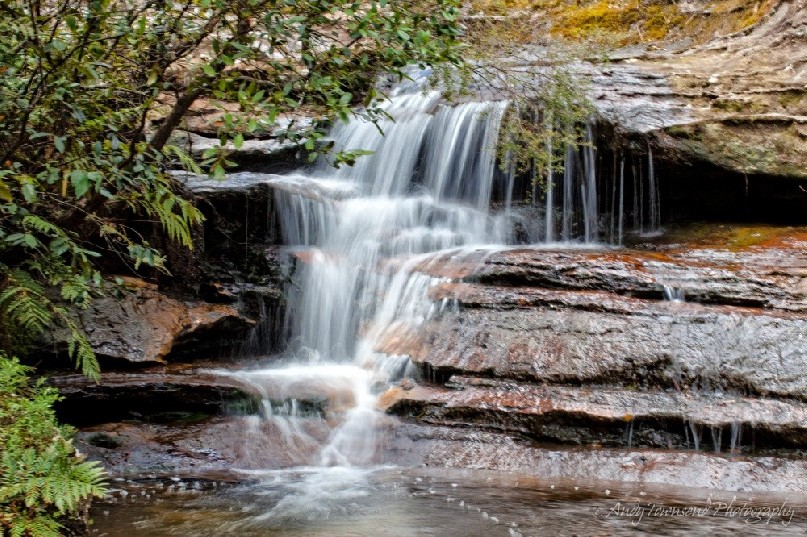 A small waterfall runs over a sandstone shelf.