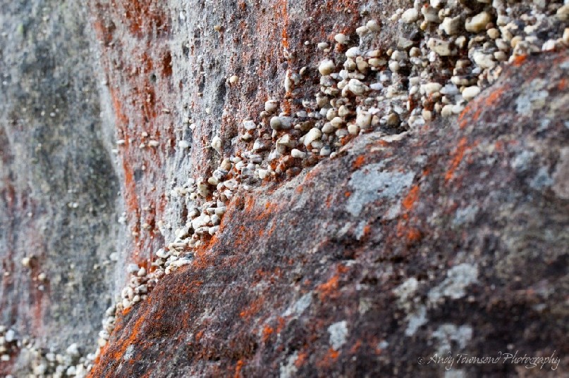 A layer of pebbles flowing through a lichen-covered sandstone wall.
