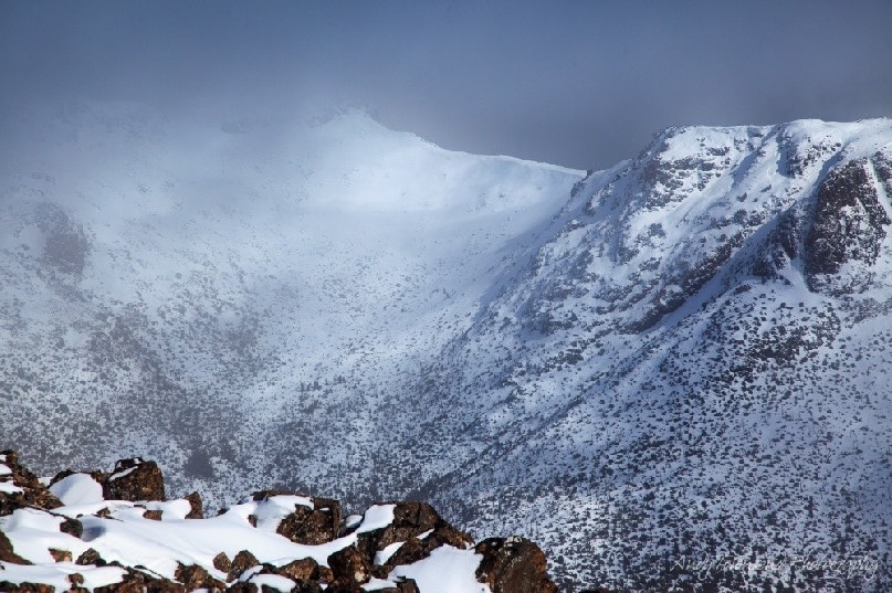 Clear clouds reveal a view to Florentine Peak covered in snow.