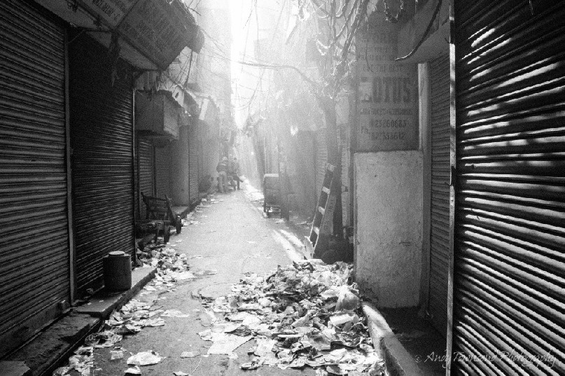 Rays of sunlight shine through chaotic electrical wiring onto a quiet alleyway.