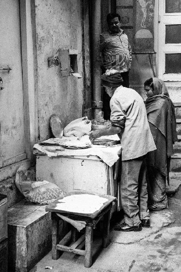 An older man and women in traditional dress making street food in alley.