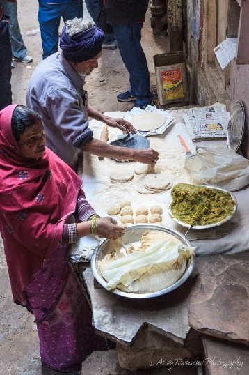 An older man and women in traditional dress making street food in alley.