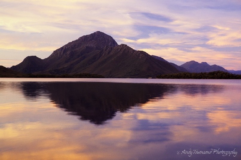 Soft evening light reflects onto the deep tannin waters of Bathurst Harbour, Southwest National Park, Tasmania.