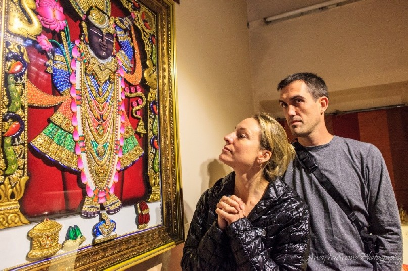A couple look at a framed embroided goddess on a wall in an old Haveli.