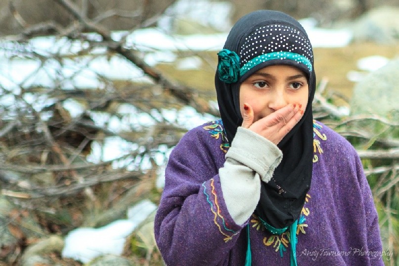 A yound Drung village girl places her hand over her mouth.