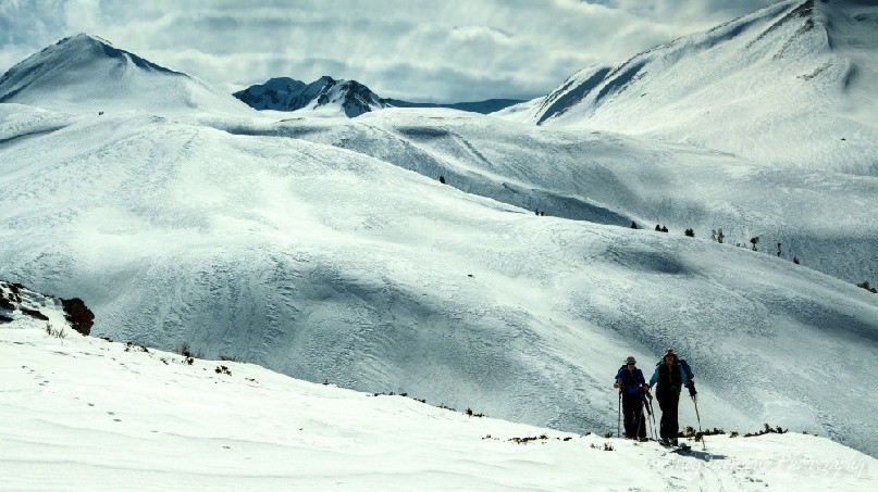 Two skiers skinning up after a run from the summit of Mt Apharwat, the distant mountain range behind.