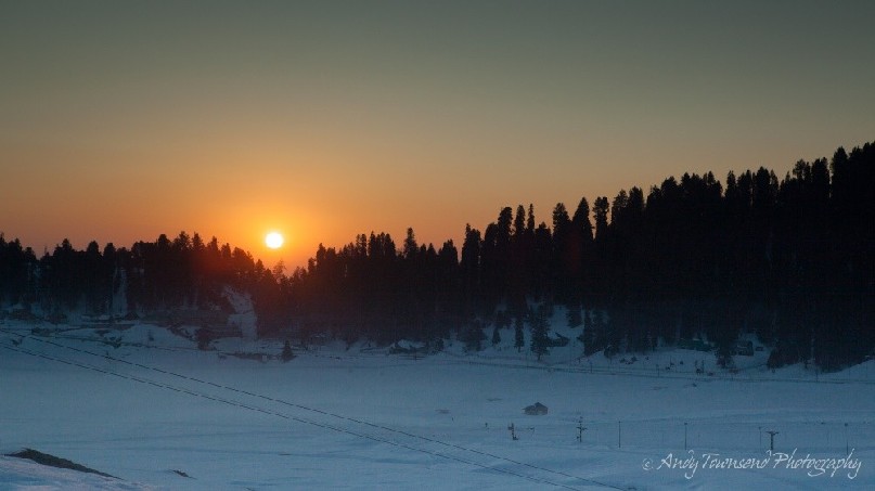 Sunlight over a forested ridge penetrates a layer of smog causes rich colours.