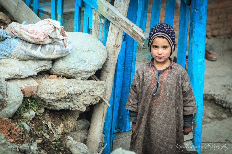 A village boy pauses for a portrait outside a blue gate near Drung village.
