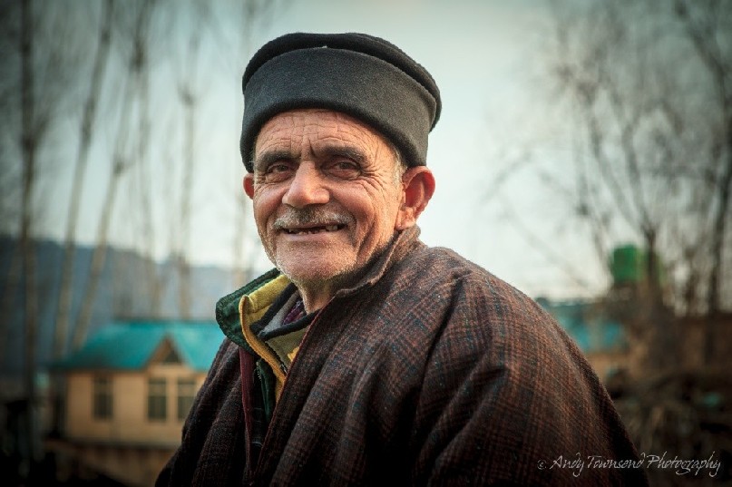 A man with craggie face sits smiling.