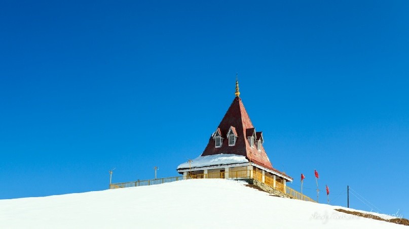 Looking up towards the Shiva temple surrounded by snow with a clear blue sky.