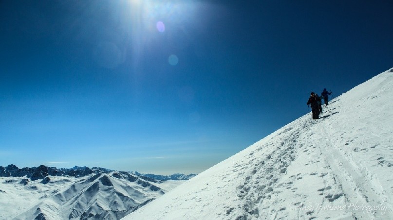 A group of skiers decent from the Shark's fin on a clear sunny day with peaks from the Pir Panjal Mountain Range beyond.