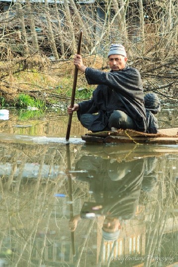 A man blances on the edge of his wooden boat navigating a channel off Dal Lake.