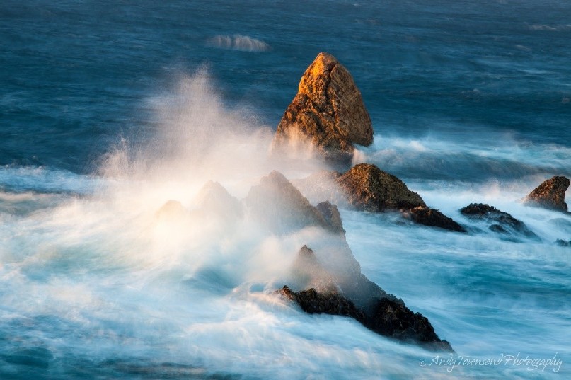 A small sea-stack on the Tarkine coast catches the last of the sun's rays as a wave crashes over it.