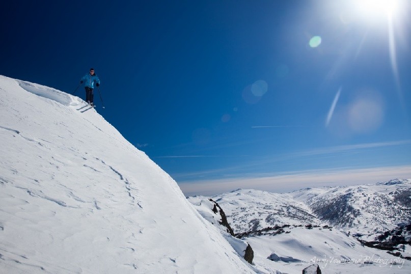 A skier drops off the edge of a small cornice on The Paralyser with a view of the Main Range in the distance, Kosciuszko National Park, Australia.