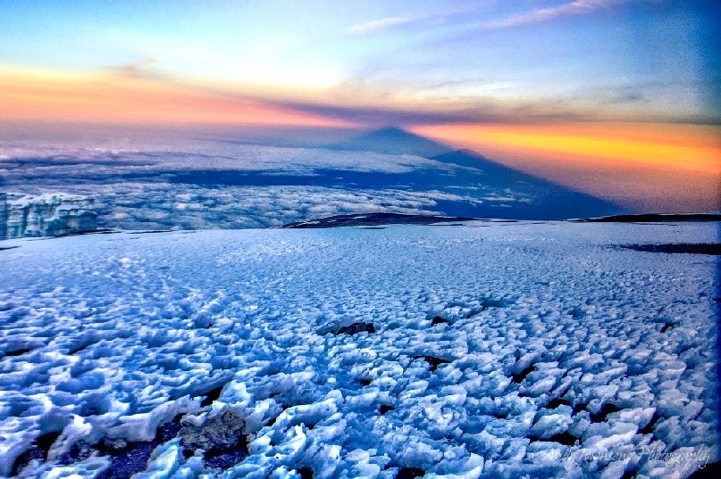 Early morning light from Mt Kilimanjaro summit with ice in the foreground and the shadow of the mountain above Mt Meru in the distance.